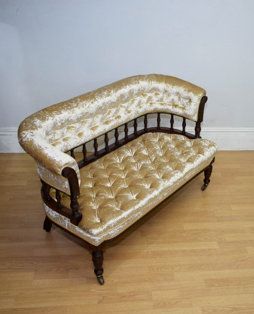A Victorian mahogany settee with champagne gold crushed velvet deep-buttoned upholstery, a spindle gallery back, and turned legs with castors. View II