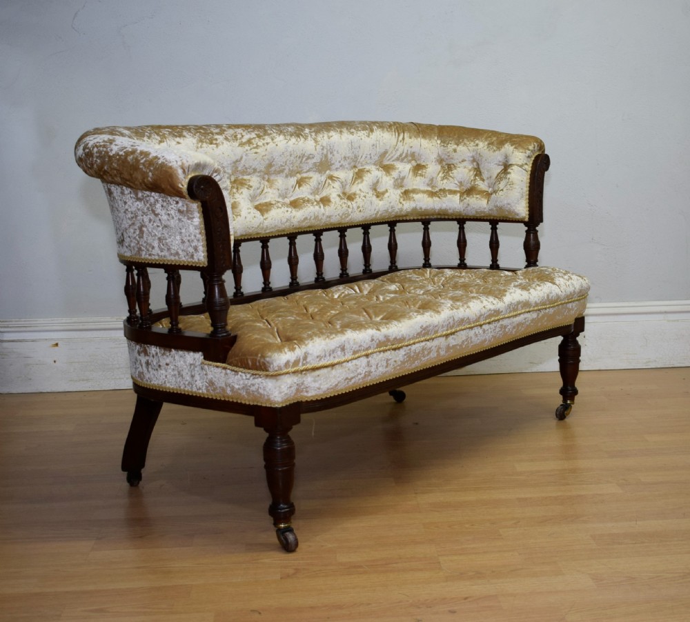 A Victorian mahogany settee with champagne gold crushed velvet deep-buttoned upholstery, a spindle gallery back, and turned legs with castors. View III