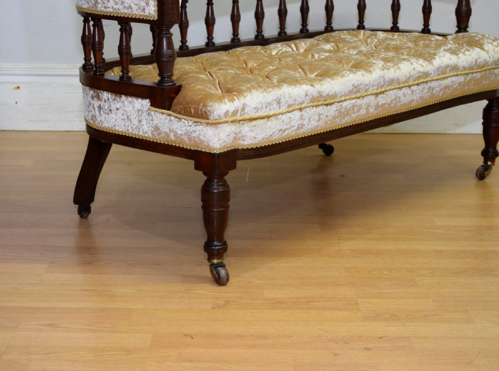 A Victorian mahogany settee with champagne gold crushed velvet deep-buttoned upholstery, a spindle gallery back, and turned legs with castors. View VI