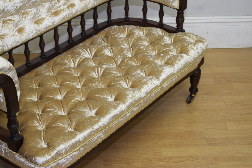 A Victorian mahogany settee with champagne gold crushed velvet deep-buttoned upholstery, a spindle gallery back, and turned legs with castors. View VII