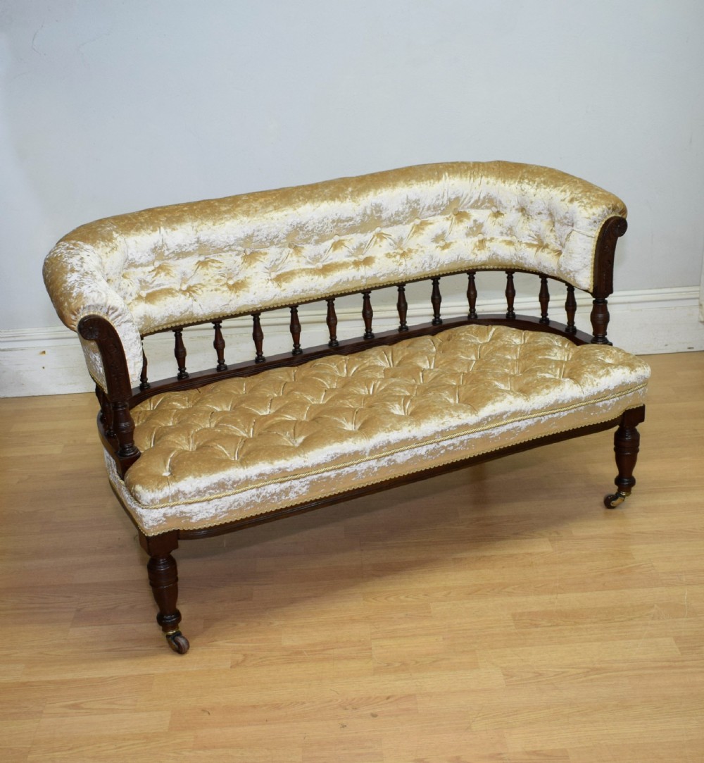 A Victorian mahogany settee with champagne gold crushed velvet deep-buttoned upholstery, a spindle gallery back, and turned legs with castors. View VIII
