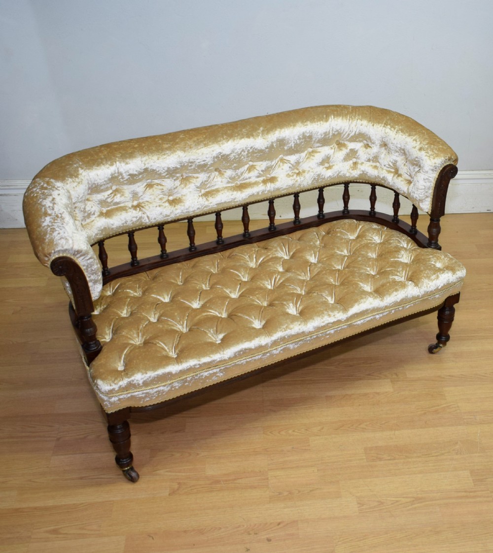 A Victorian mahogany settee with champagne gold crushed velvet deep-buttoned upholstery, a spindle gallery back, and turned legs with castors. View IX