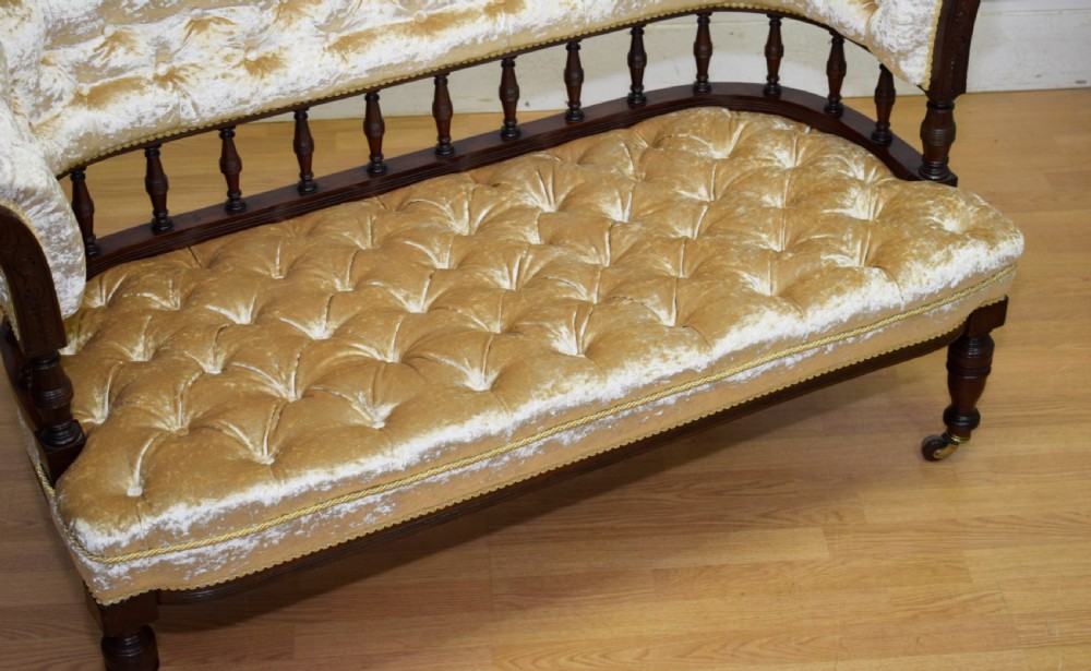 A Victorian mahogany settee with champagne gold crushed velvet deep-buttoned upholstery, a spindle gallery back, and turned legs with castors. View X