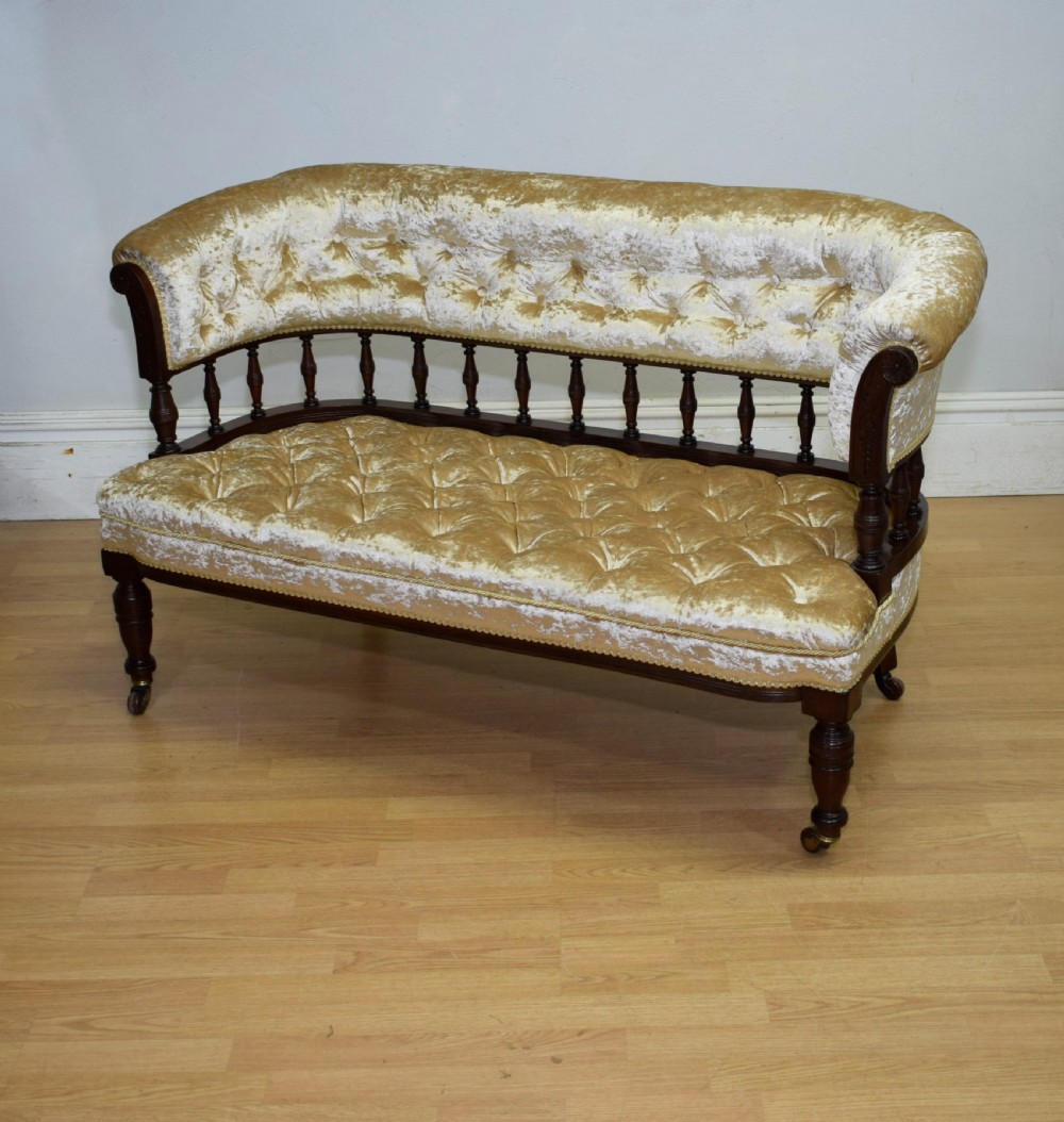 A Victorian mahogany settee with champagne gold crushed velvet deep-buttoned upholstery, a spindle gallery back, and turned legs with castors. View XI