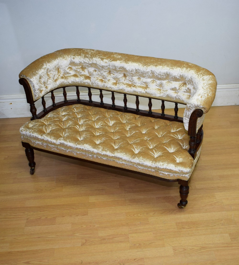 A Victorian mahogany settee with champagne gold crushed velvet deep-buttoned upholstery, a spindle gallery back, and turned legs with castors. View XII