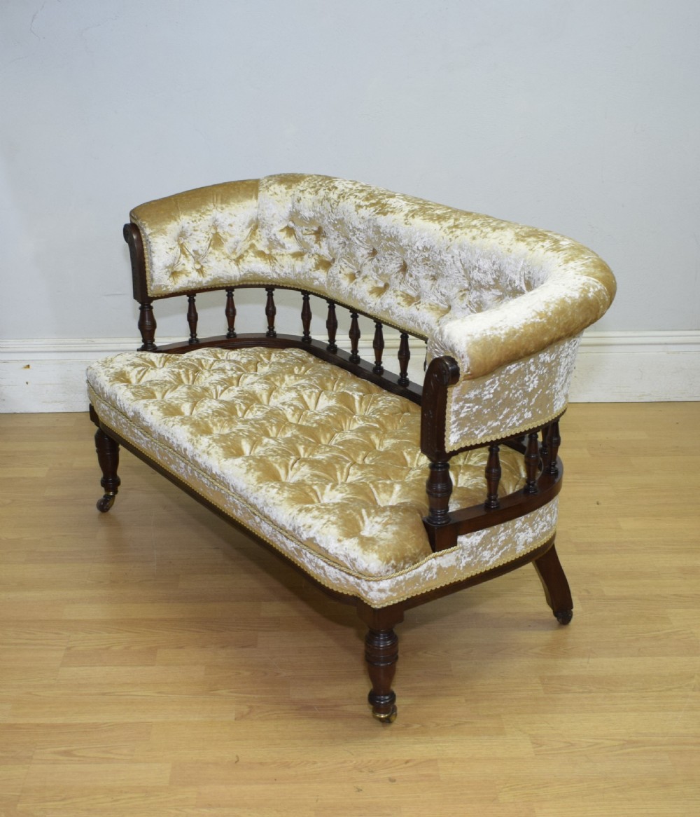 A Victorian mahogany settee with champagne gold crushed velvet deep-buttoned upholstery, a spindle gallery back, and turned legs with castors. View XIII