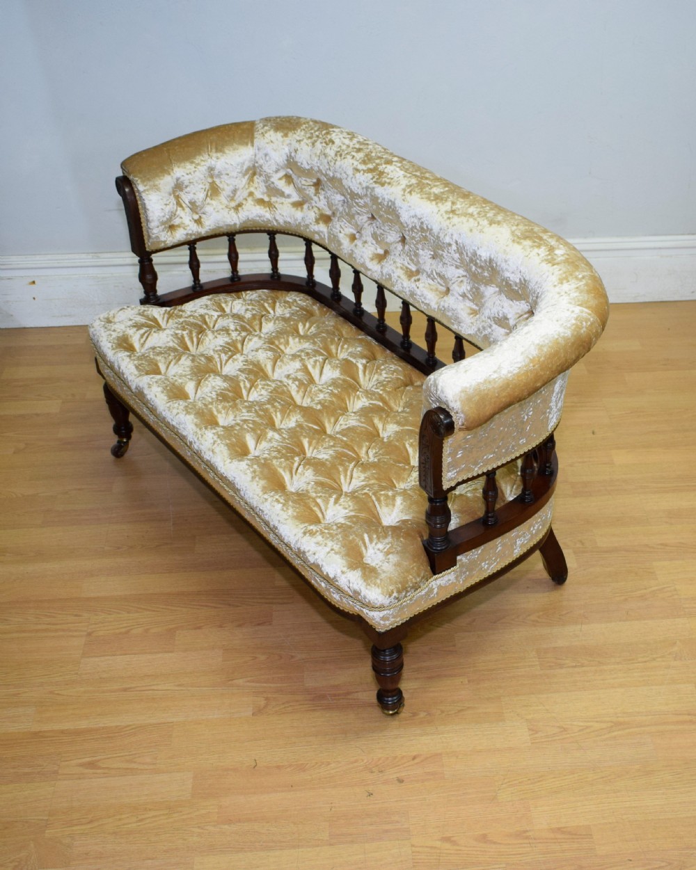 A Victorian mahogany settee with champagne gold crushed velvet deep-buttoned upholstery, a spindle gallery back, and turned legs with castors. View XV