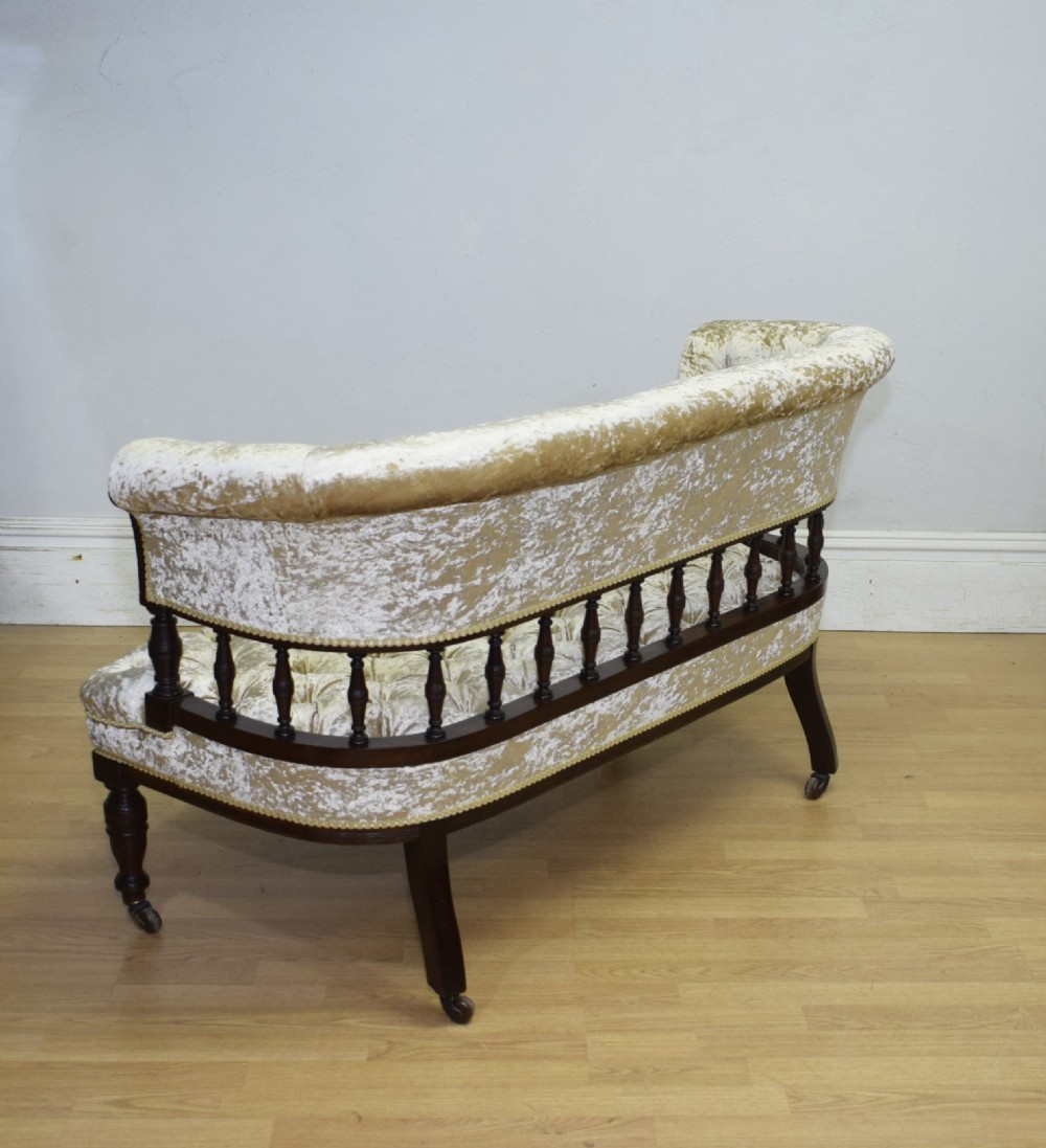 A Victorian mahogany settee with champagne gold crushed velvet deep-buttoned upholstery, a spindle gallery back, and turned legs with castors. View XVI