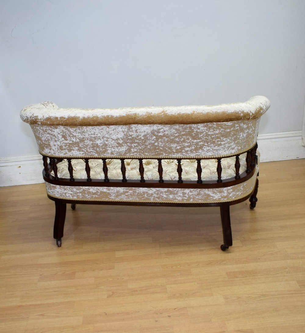 A Victorian mahogany settee with champagne gold crushed velvet deep-buttoned upholstery, a spindle gallery back, and turned legs with castors. View XVII