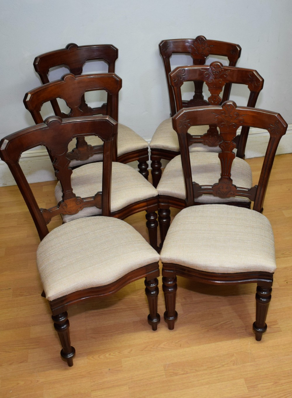 A set of six Victorian mahogany dining chairs featuring carved open backs, turned front legs, and neutral upholstered seats. View X