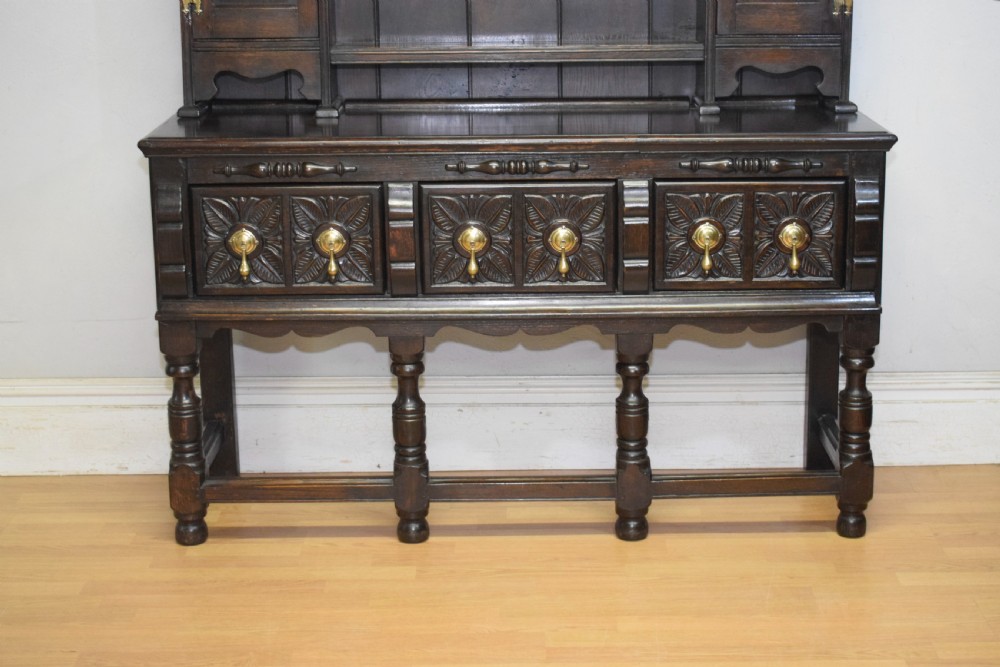 A dark carved oak Jacobean style Welsh dresser featuring an upper plate rack with side cupboard doors over a lower sideboard base with three carved drawers and turned legs. View III