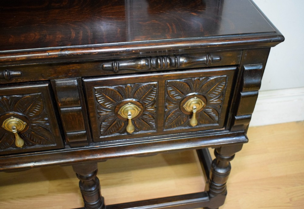 A dark carved oak Jacobean style Welsh dresser featuring an upper plate rack with side cupboard doors over a lower sideboard base with three carved drawers and turned legs. View IX