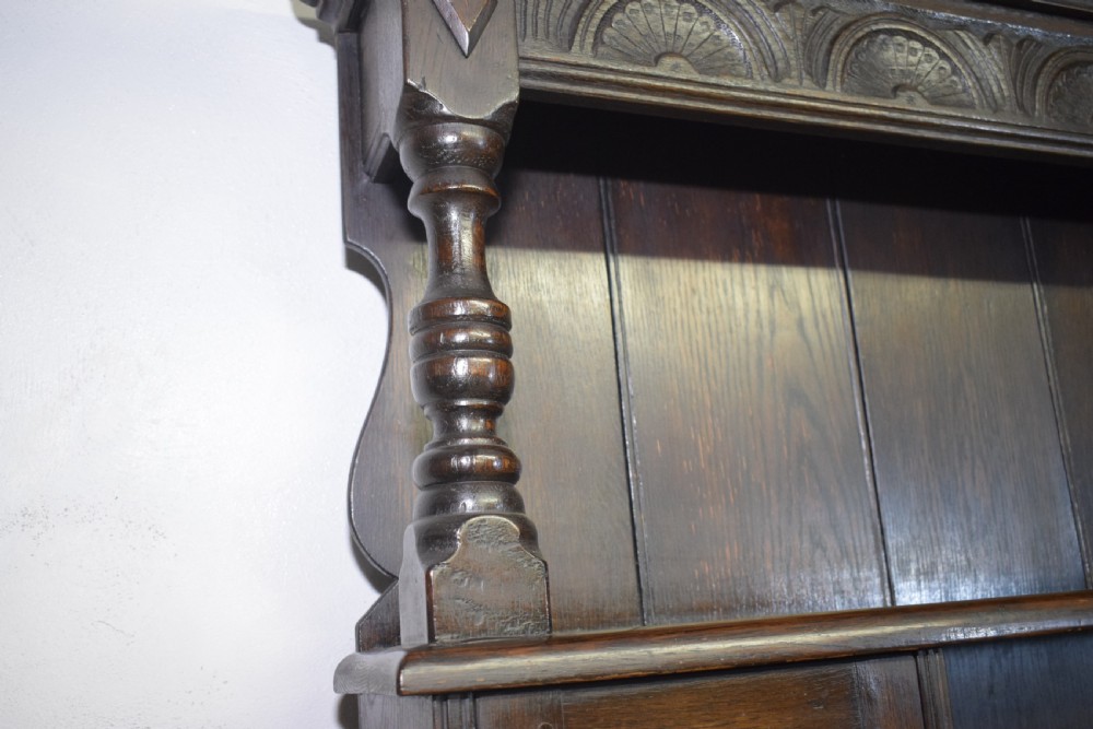 A dark carved oak Jacobean style Welsh dresser featuring an upper plate rack with side cupboard doors over a lower sideboard base with three carved drawers and turned legs. View X
