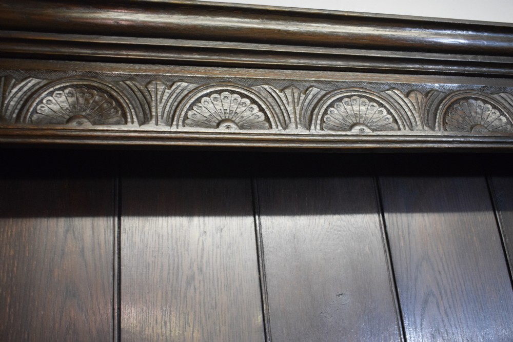 A dark carved oak Jacobean style Welsh dresser featuring an upper plate rack with side cupboard doors over a lower sideboard base with three carved drawers and turned legs. View XI