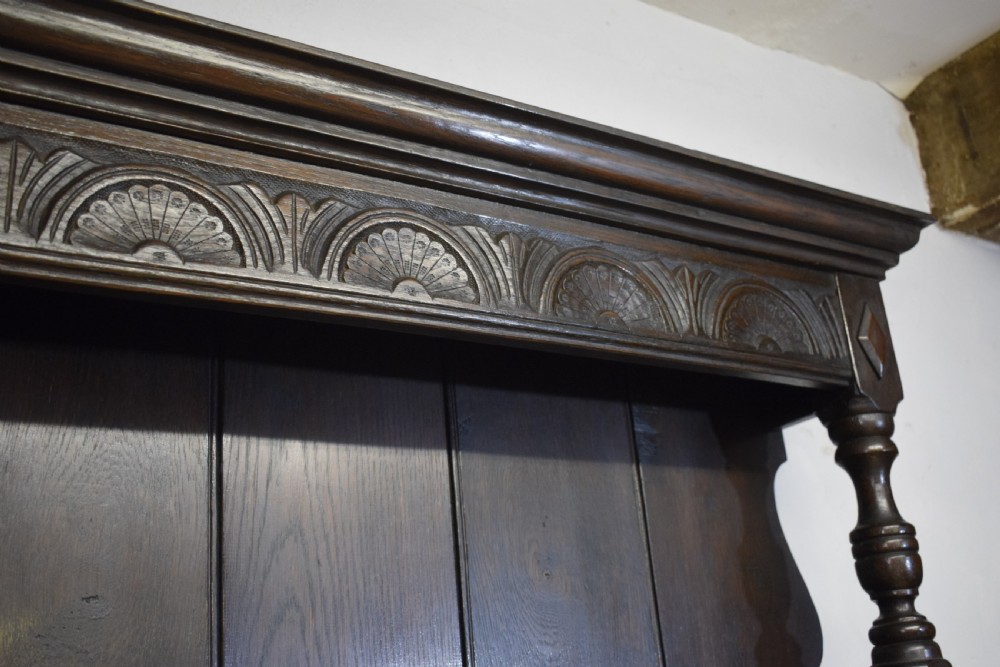 A dark carved oak Jacobean style Welsh dresser featuring an upper plate rack with side cupboard doors over a lower sideboard base with three carved drawers and turned legs. View XII
