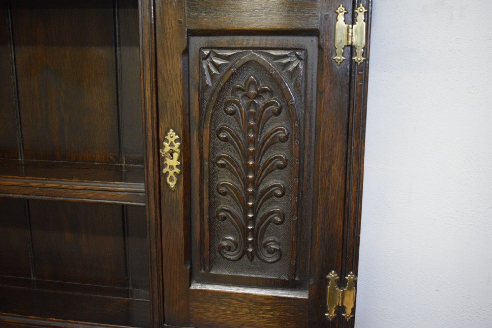 A dark carved oak Jacobean style Welsh dresser featuring an upper plate rack with side cupboard doors over a lower sideboard base with three carved drawers and turned legs. View XIII