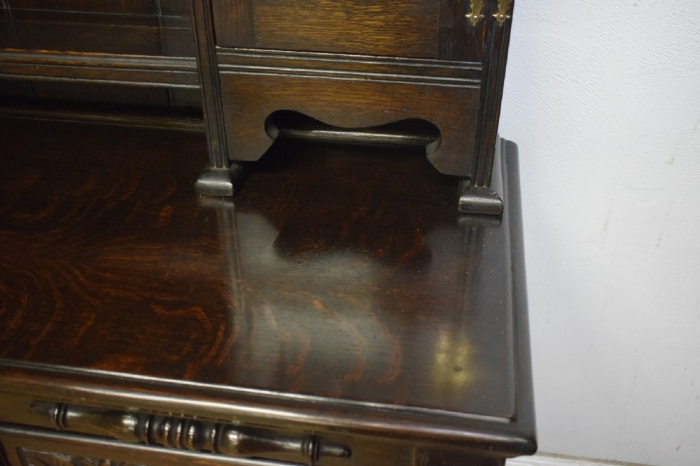 A dark carved oak Jacobean style Welsh dresser featuring an upper plate rack with side cupboard doors over a lower sideboard base with three carved drawers and turned legs. View XIV