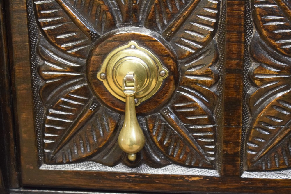 A dark carved oak Jacobean style Welsh dresser featuring an upper plate rack with side cupboard doors over a lower sideboard base with three carved drawers and turned legs. View XV
