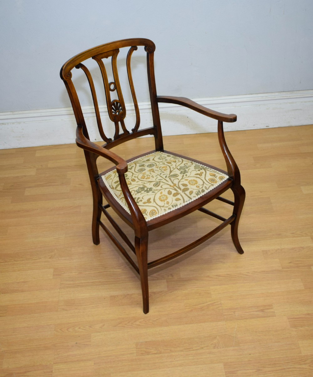An Edwardian mahogany open armchair featuring a carved splat back, shaped armrests, and floral pattern fabric upholstery.