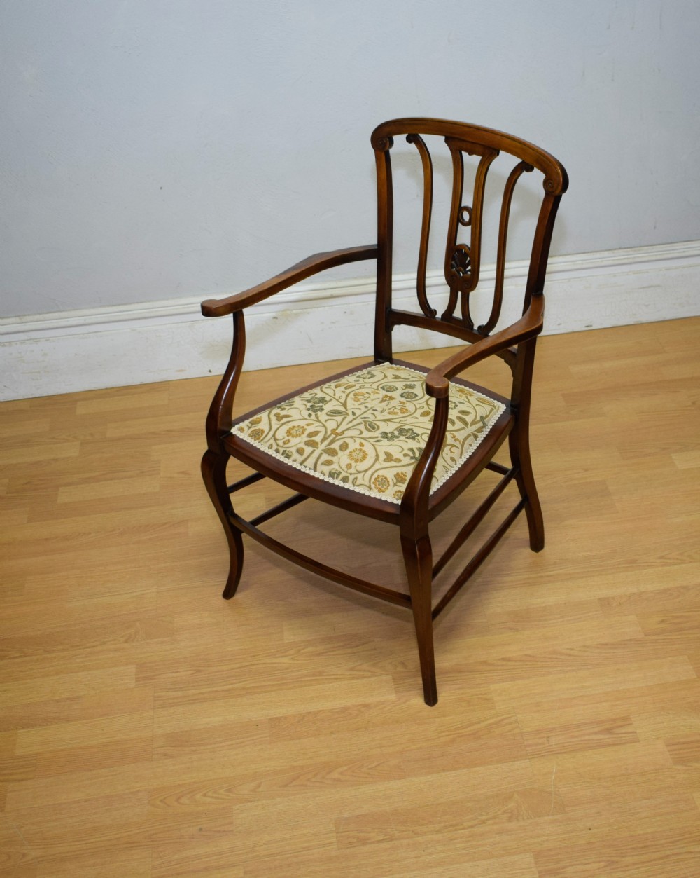 An Edwardian mahogany open armchair featuring a carved splat back, shaped armrests, and floral pattern fabric upholstery. View V