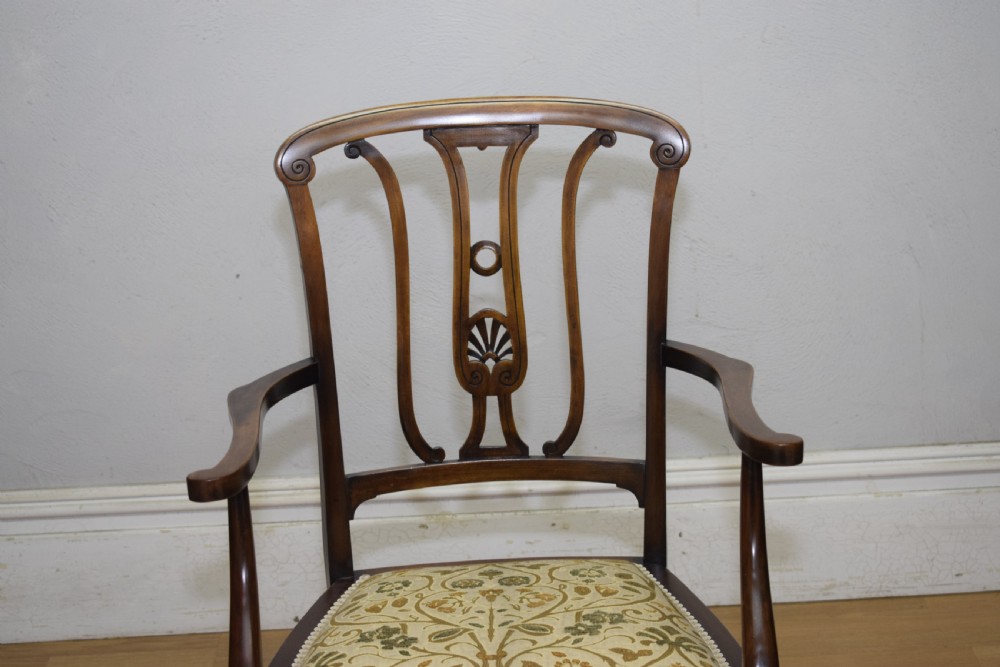 An Edwardian mahogany open armchair featuring a carved splat back, shaped armrests, and floral pattern fabric upholstery. View X