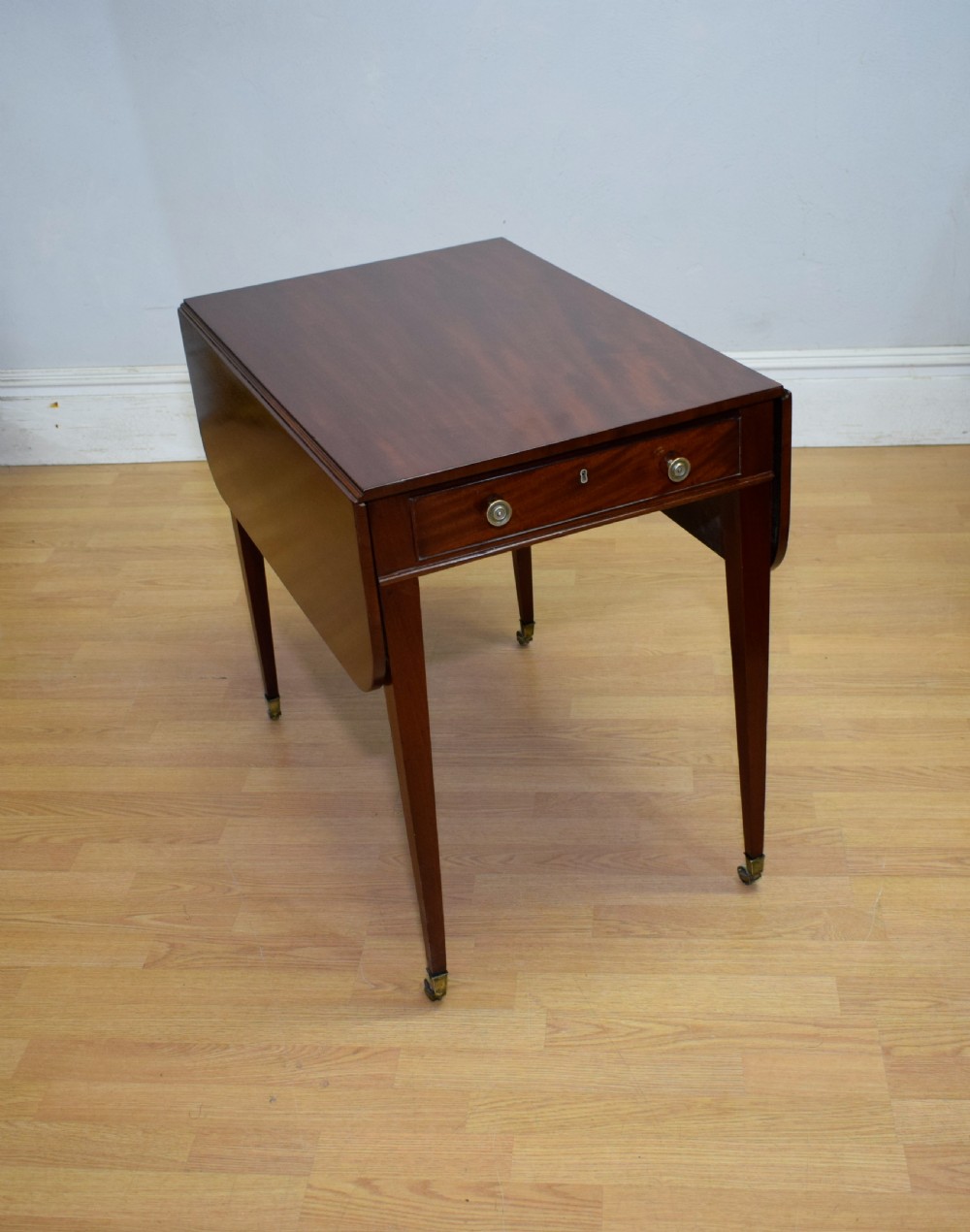 A Regency mahogany Pembroke table featuring dual drop-leaf sides, a front drawer with two brass pull knobs, square tapered legs, and brass brass castors. View II