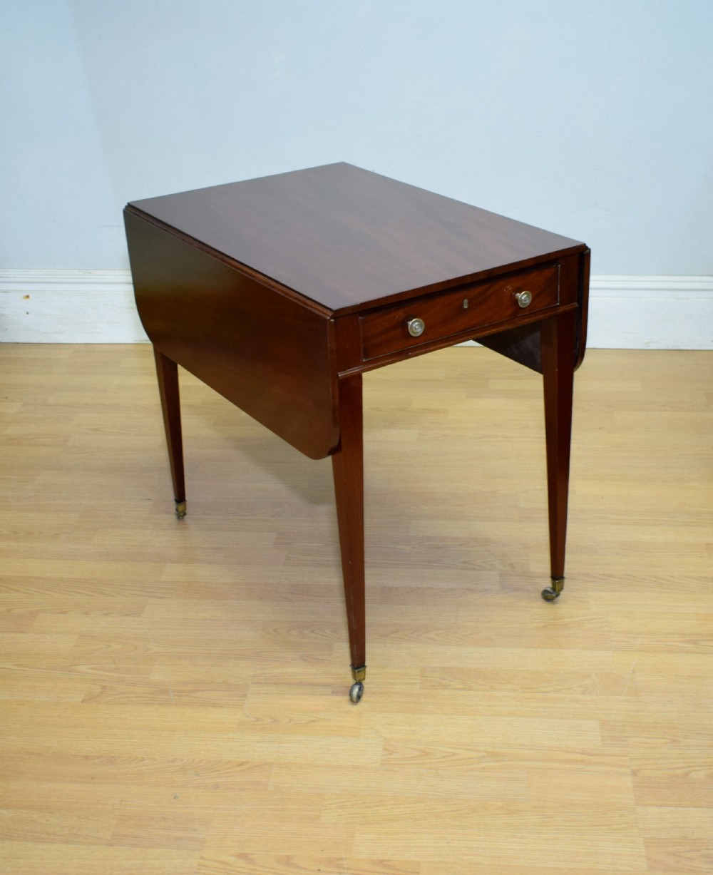 A Regency mahogany Pembroke table featuring dual drop-leaf sides, a front drawer with two brass pull knobs, square tapered legs, and brass brass castors. View VI
