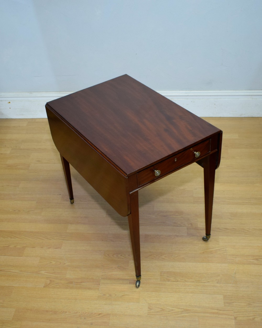 A Regency mahogany Pembroke table featuring dual drop-leaf sides, a front drawer with two brass pull knobs, square tapered legs, and brass brass castors. View VII