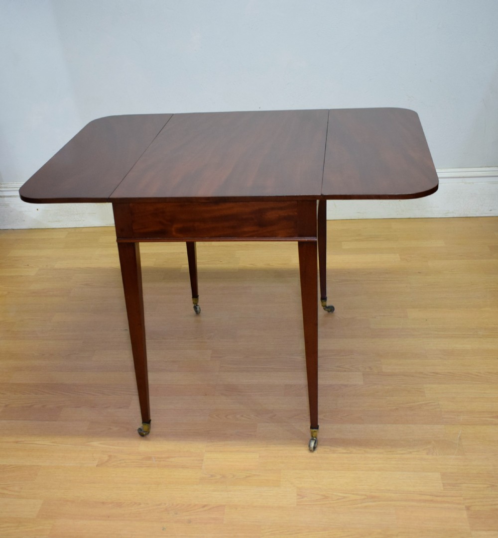 A Regency mahogany Pembroke table featuring dual drop-leaf sides, a front drawer with two brass pull knobs, square tapered legs, and brass brass castors. View IX