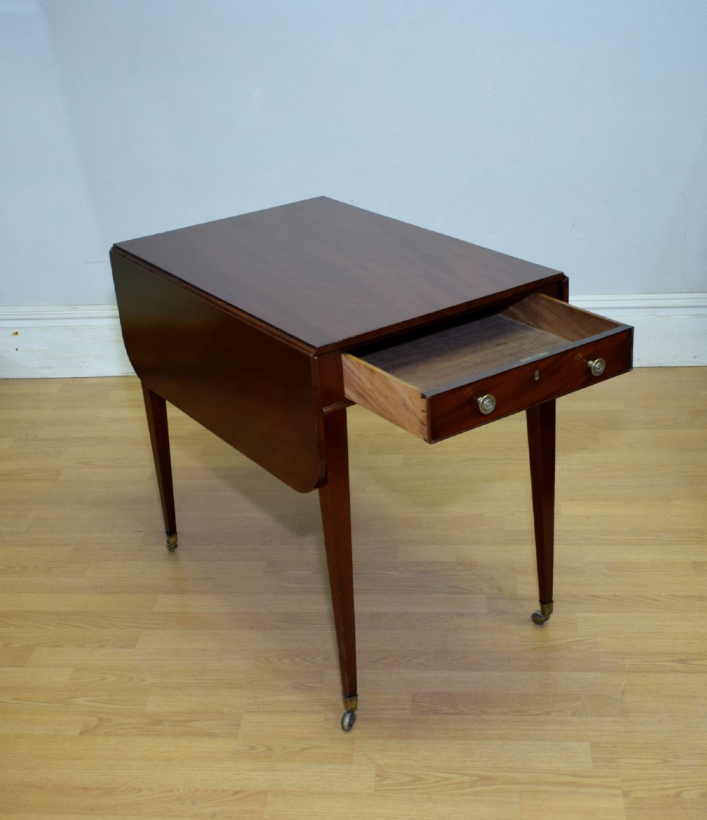 A Regency mahogany Pembroke table featuring dual drop-leaf sides, a front drawer with two brass pull knobs, square tapered legs, and brass brass castors. View X