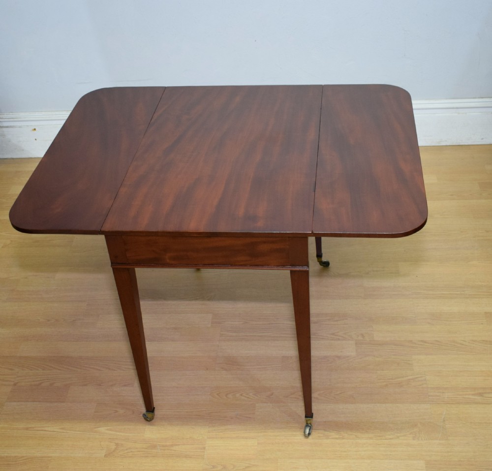 A Regency mahogany Pembroke table featuring dual drop-leaf sides, a front drawer with two brass pull knobs, square tapered legs, and brass brass castors. View XI