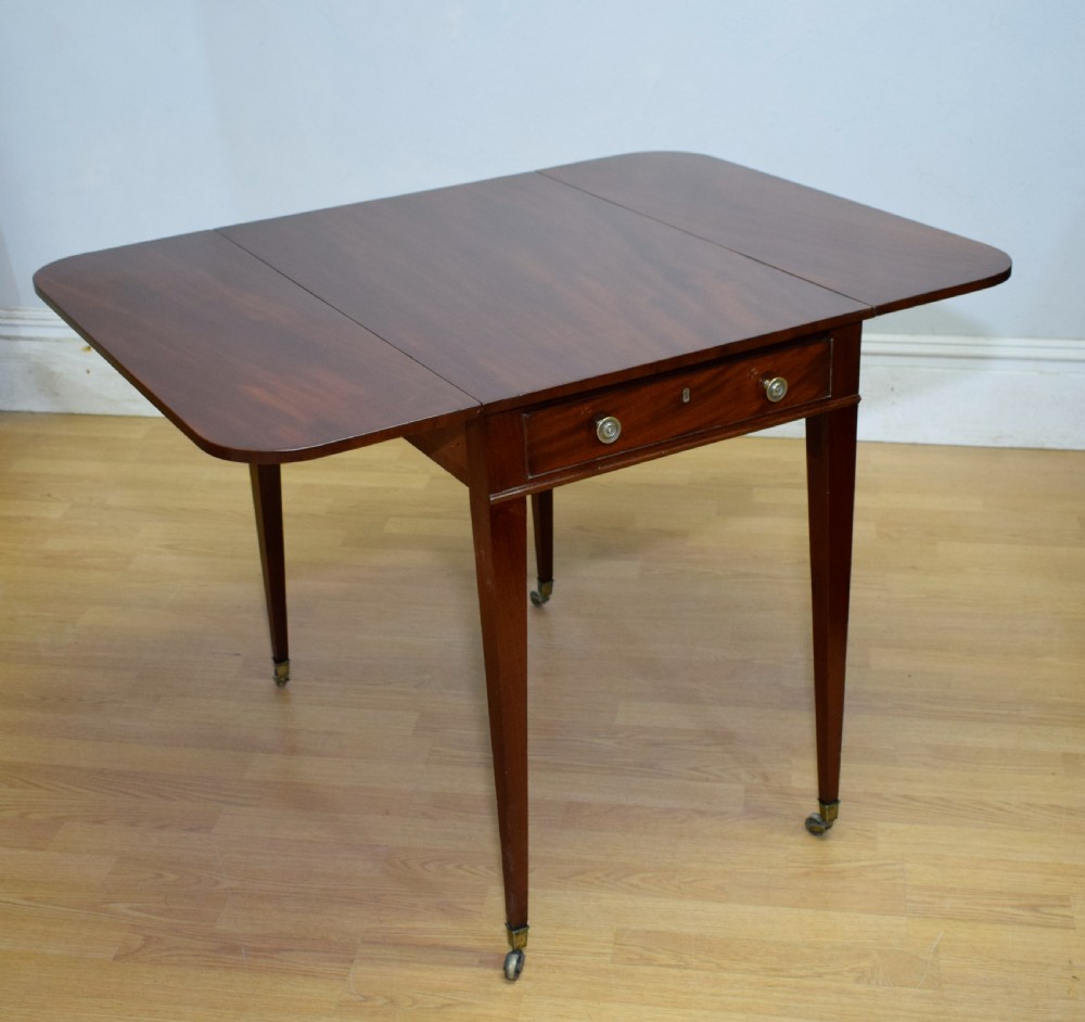 A Regency mahogany Pembroke table featuring dual drop-leaf sides, a front drawer with two brass pull knobs, square tapered legs, and brass brass castors. View XV