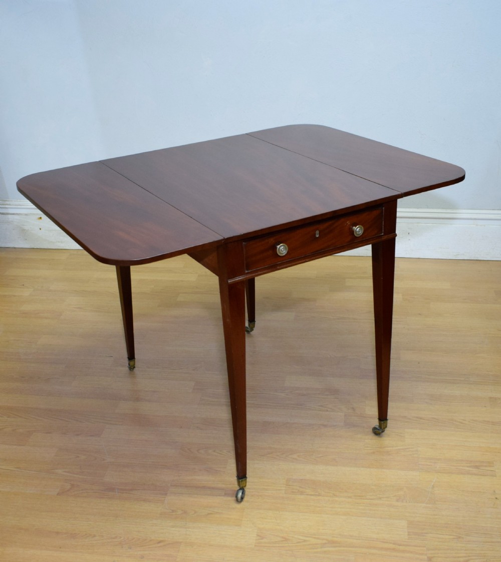 A Regency mahogany Pembroke table featuring dual drop-leaf sides, a front drawer with two brass pull knobs, square tapered legs, and brass brass castors. View XVII