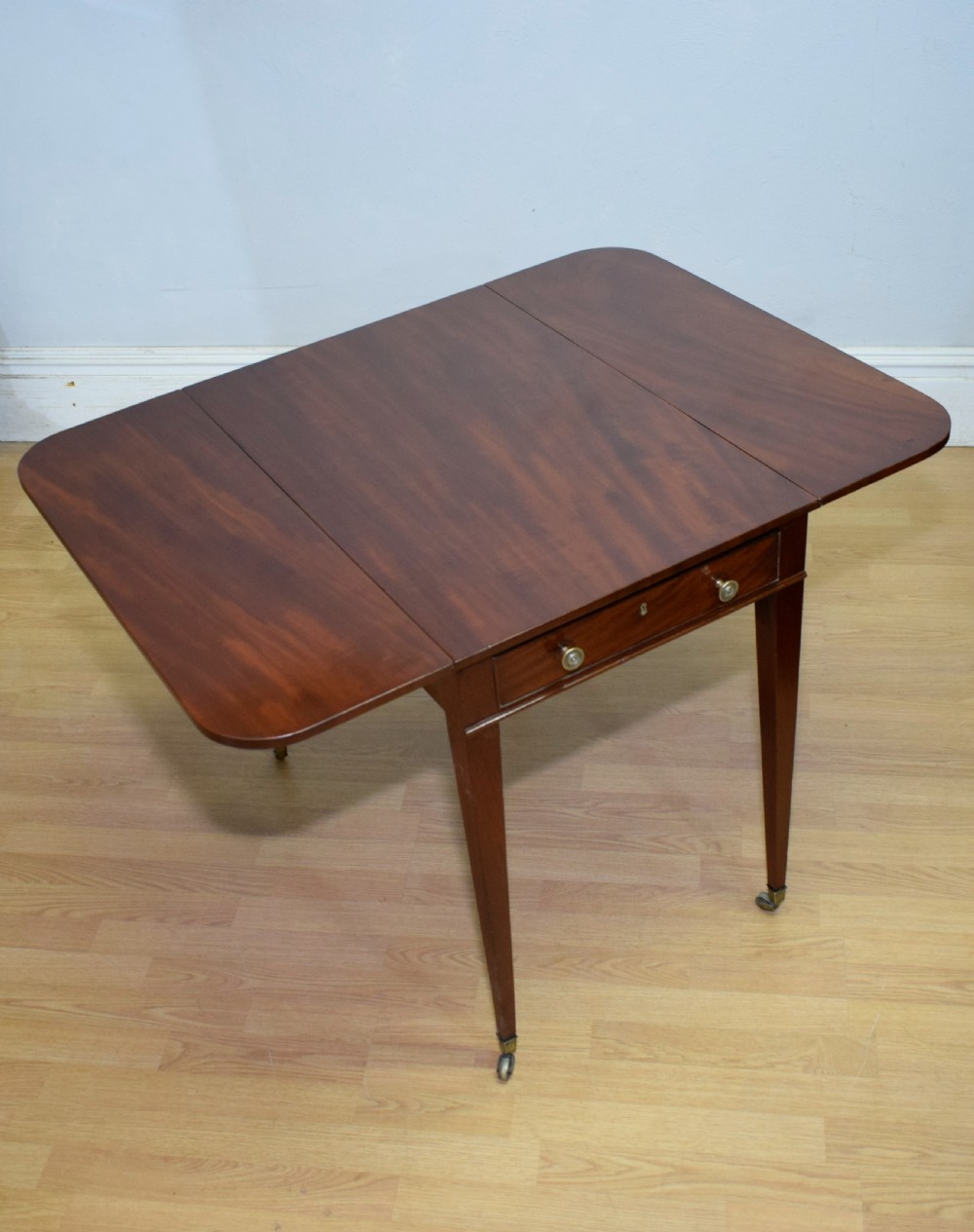 A Regency mahogany Pembroke table featuring dual drop-leaf sides, a front drawer with two brass pull knobs, square tapered legs, and brass brass castors. View XVIII