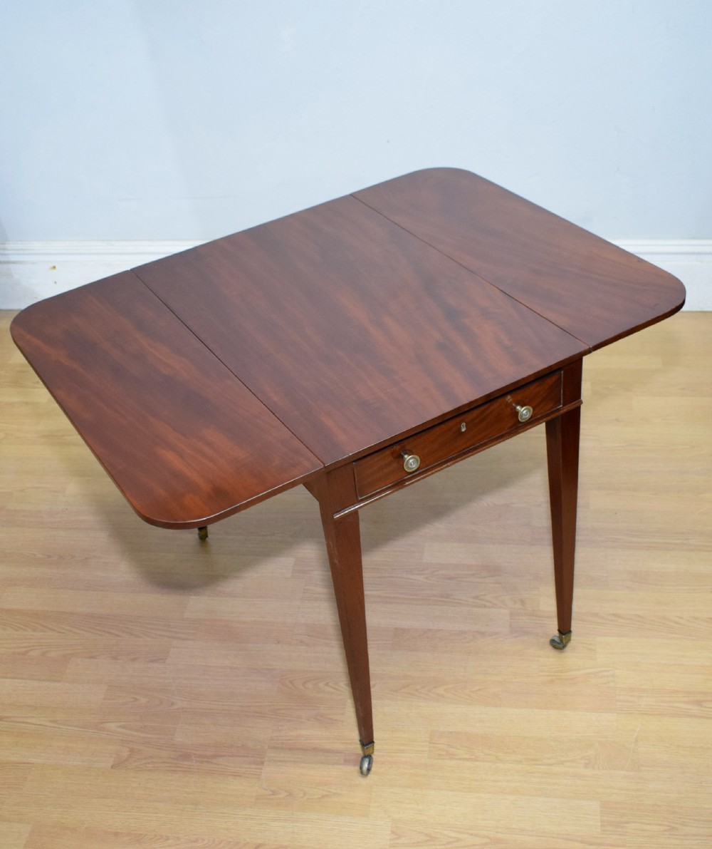 A Regency mahogany Pembroke table featuring dual drop-leaf sides, a front drawer with two brass pull knobs, square tapered legs, and brass brass castors. View XIX