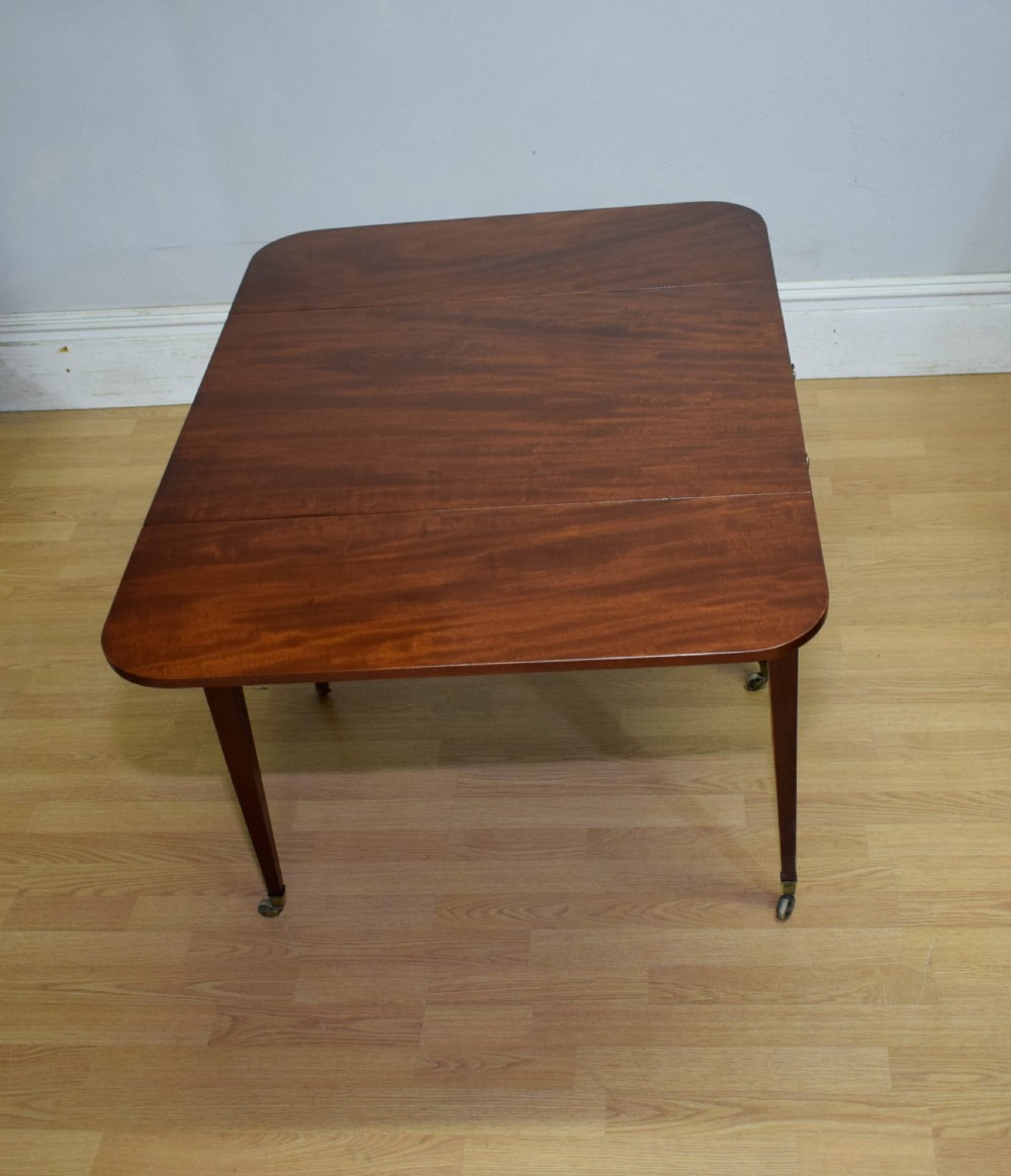 A Regency mahogany Pembroke table featuring dual drop-leaf sides, a front drawer with two brass pull knobs, square tapered legs, and brass brass castors. View XX