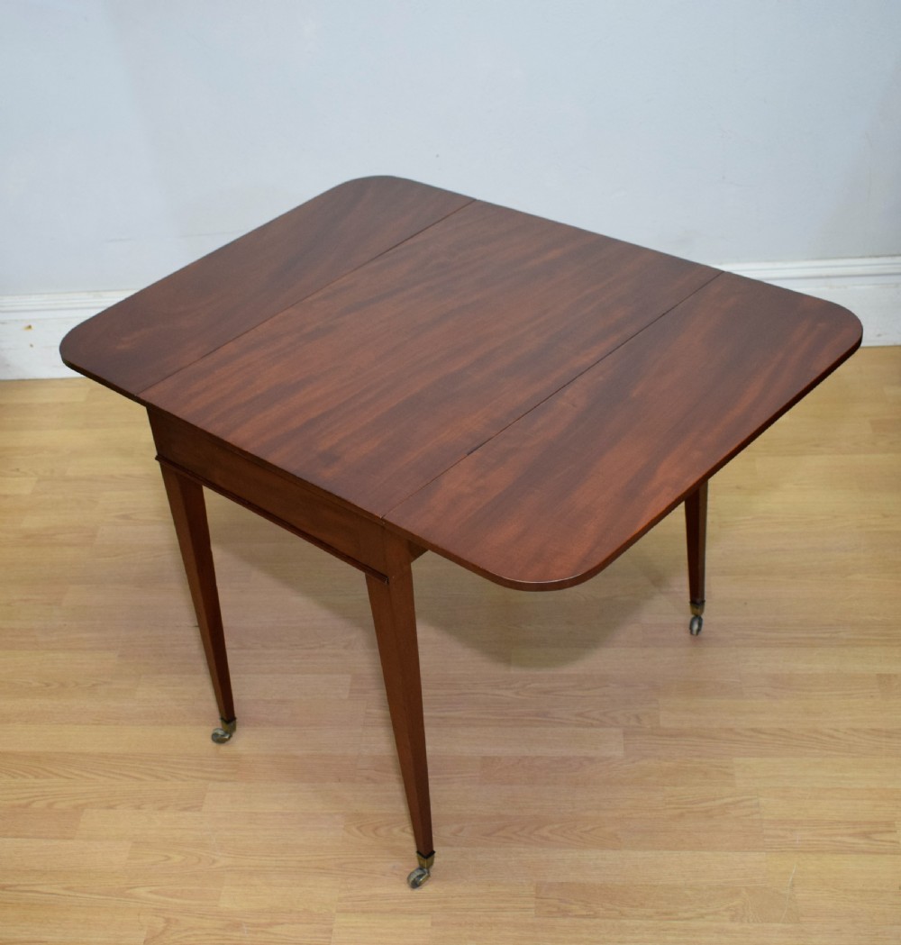 A Regency mahogany Pembroke table featuring dual drop-leaf sides, a front drawer with two brass pull knobs, square tapered legs, and brass brass castors. View XXII