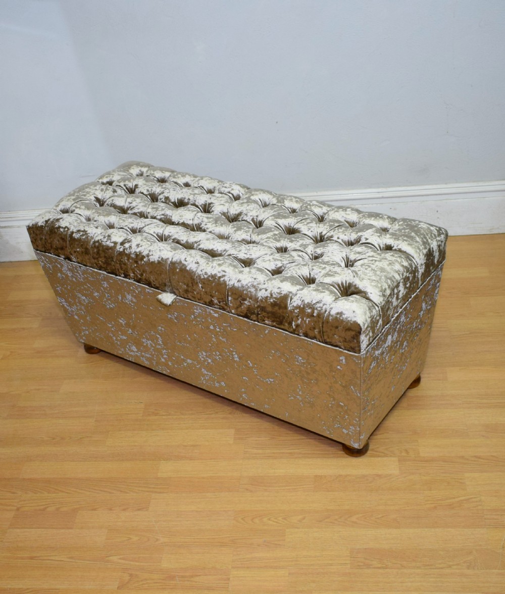 A rectangular upholstered storage ottoman in champagne crushed velvet with a deep buttoned tufted lid and small wooden feet.