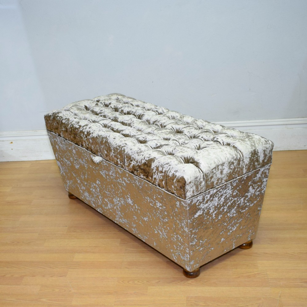 A rectangular upholstered storage ottoman in champagne crushed velvet with a deep buttoned tufted lid and small wooden feet. View VII