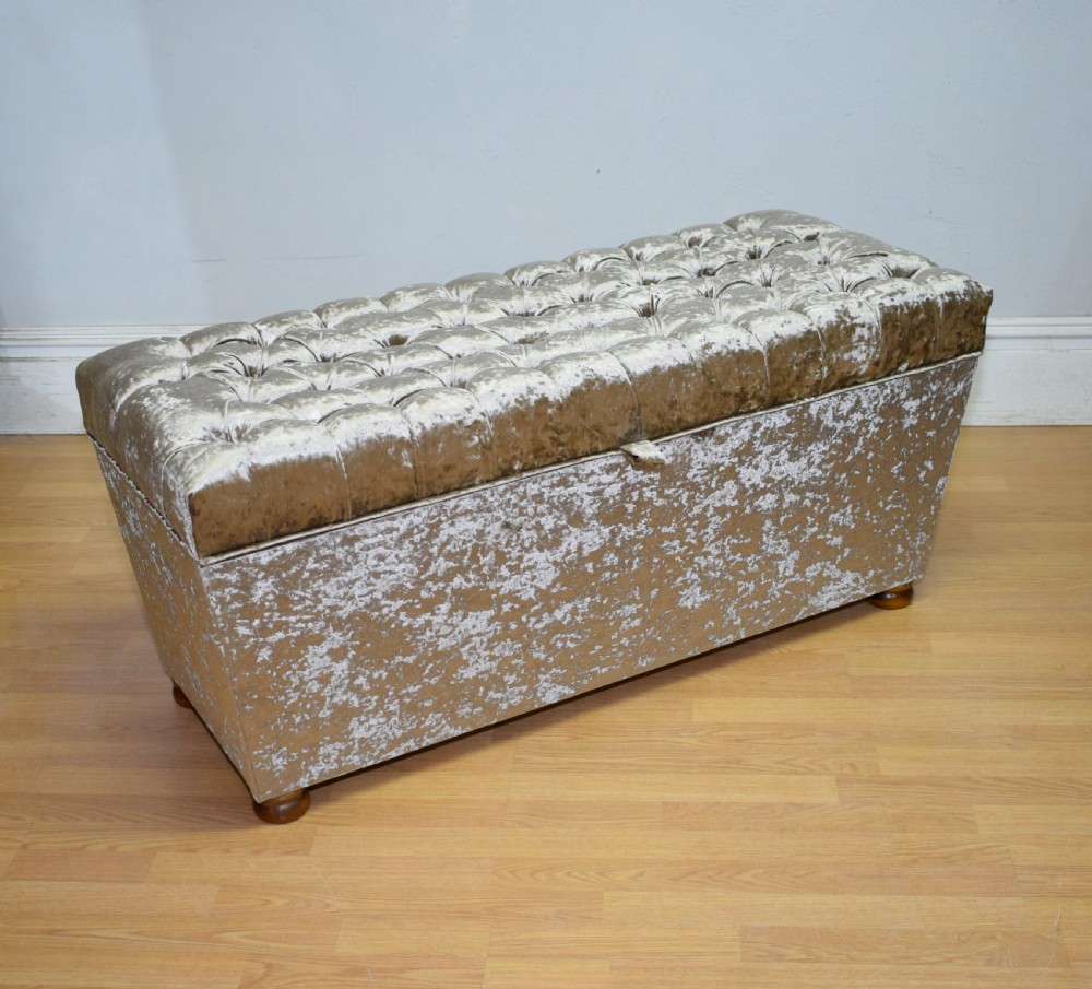 A rectangular upholstered storage ottoman in champagne crushed velvet with a deep buttoned tufted lid and small wooden feet. View IX