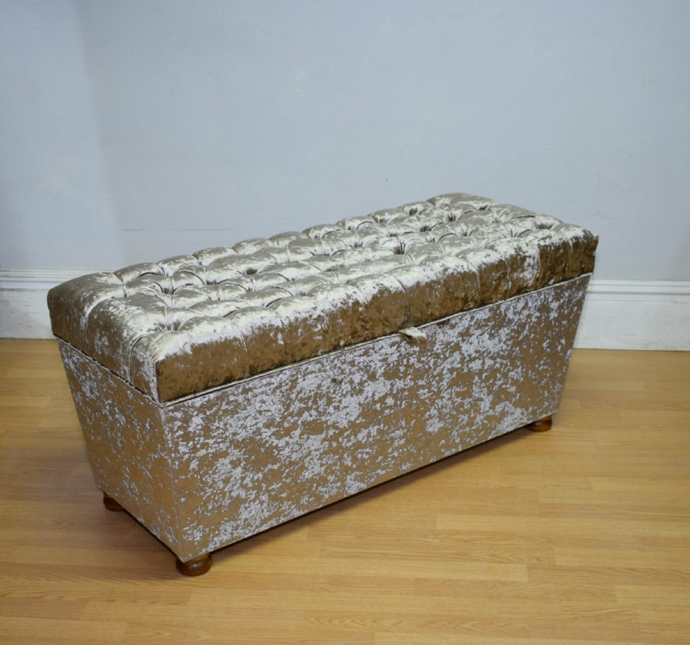 A rectangular upholstered storage ottoman in champagne crushed velvet with a deep buttoned tufted lid and small wooden feet. View X