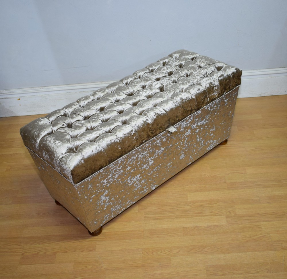 A rectangular upholstered storage ottoman in champagne crushed velvet with a deep buttoned tufted lid and small wooden feet. View XI