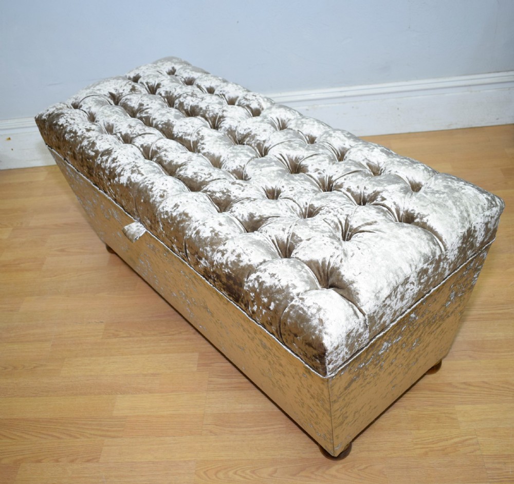 A rectangular upholstered storage ottoman in champagne crushed velvet with a deep buttoned tufted lid and small wooden feet. View XIII