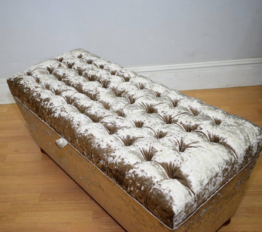 A rectangular upholstered storage ottoman in champagne crushed velvet with a deep buttoned tufted lid and small wooden feet. View XV