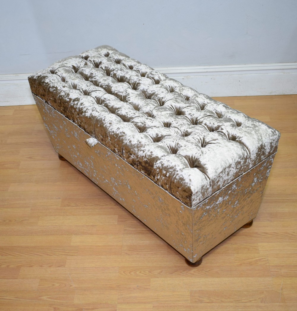 A rectangular upholstered storage ottoman in champagne crushed velvet with a deep buttoned tufted lid and small wooden feet. View XVI