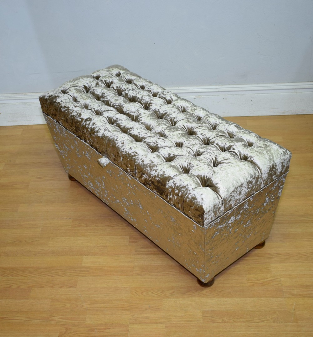 A rectangular upholstered storage ottoman in champagne crushed velvet with a deep buttoned tufted lid and small wooden feet. View XVII