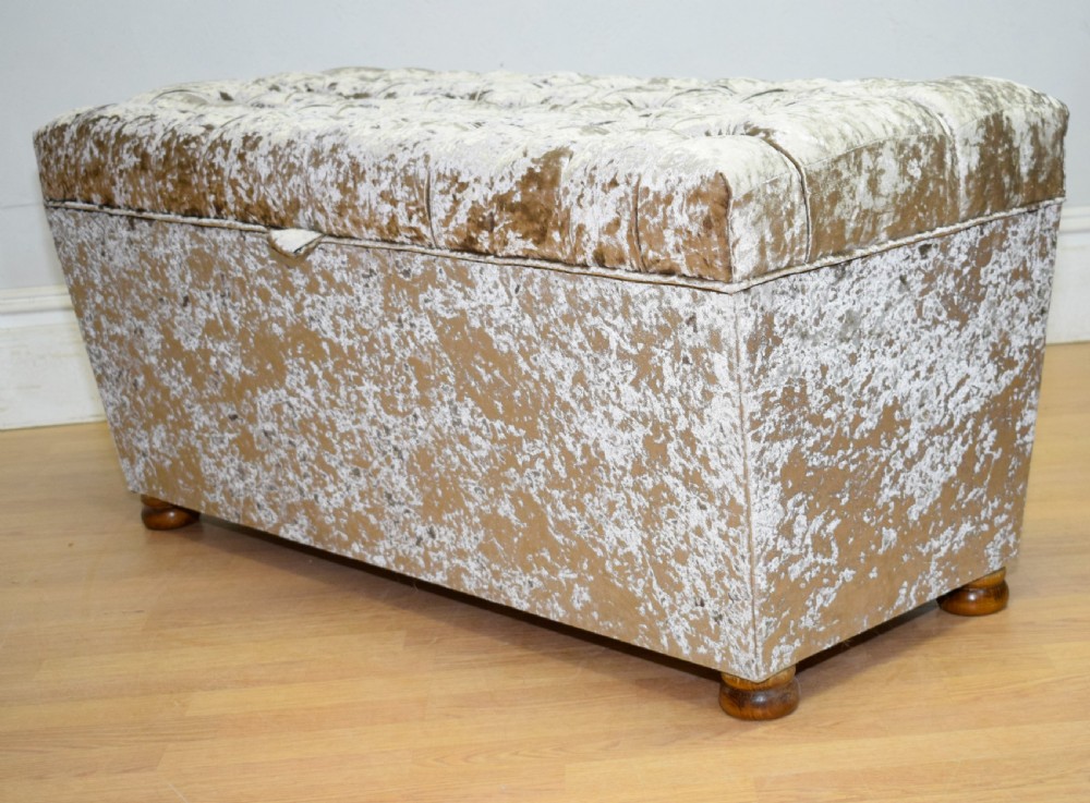 A rectangular upholstered storage ottoman in champagne crushed velvet with a deep buttoned tufted lid and small wooden feet. View XIX