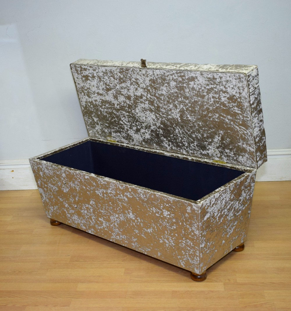 A rectangular upholstered storage ottoman in champagne crushed velvet with a deep buttoned tufted lid and small wooden feet. View XX