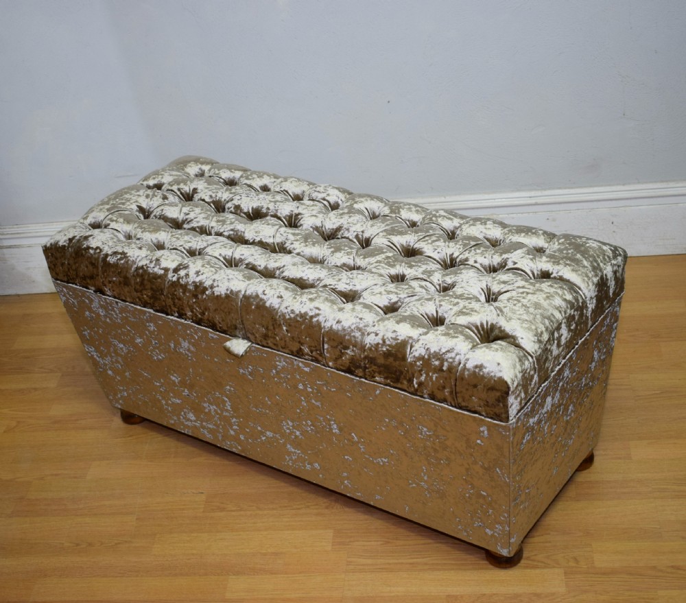 A rectangular upholstered storage ottoman in champagne crushed velvet with a deep buttoned tufted lid and small wooden feet. View XXI