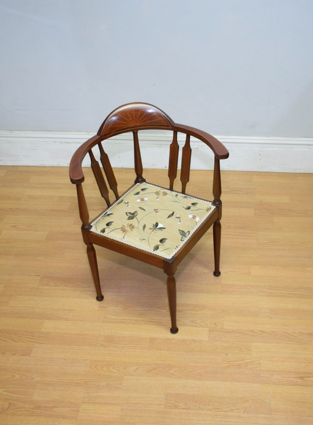 An Edwardian mahogany corner chair featuring a curved top rail with fan inlay, turned spindles, and a floral upholstered square seat.